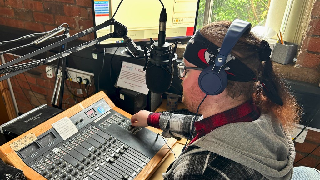 Connor Lewins in the studio presenting a show. He is adjusting the music settings as he prepares to speak to the audience. 