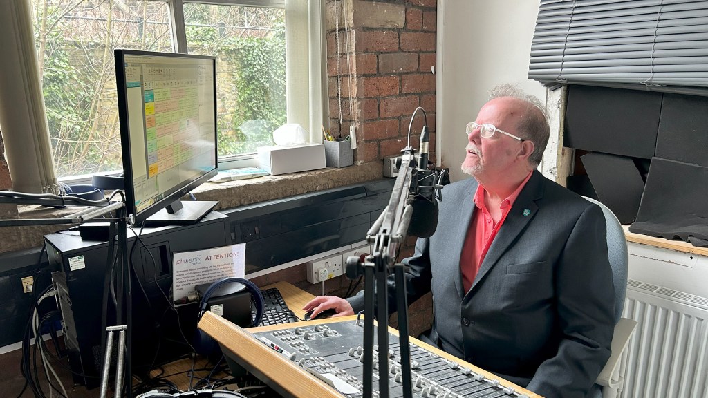 Phoenix FM's manager, Howard Priestley, at the desk of the old studio. The studio looks disheveled, emphasising Phoenix's situation.  